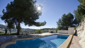 Una piscina con vistas al campo, rodeada de árboles y un muro blanco.