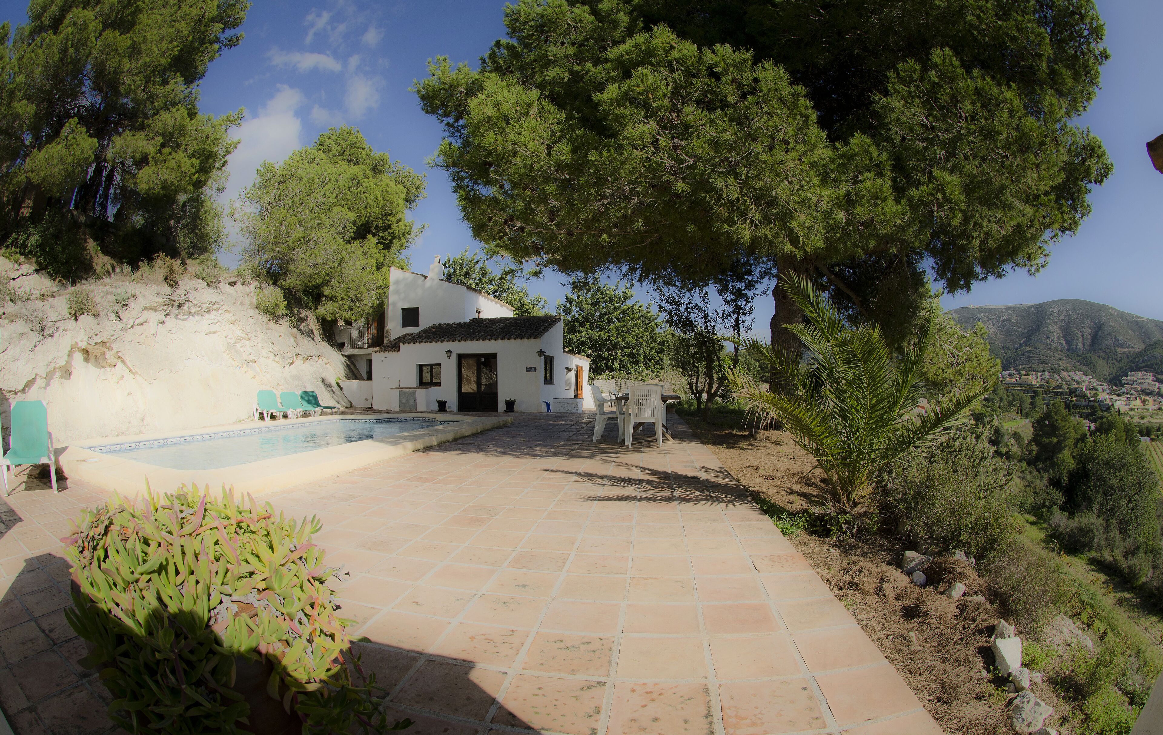 A white villa with a swimming pool, surrounded by trees and a view of the hills.
