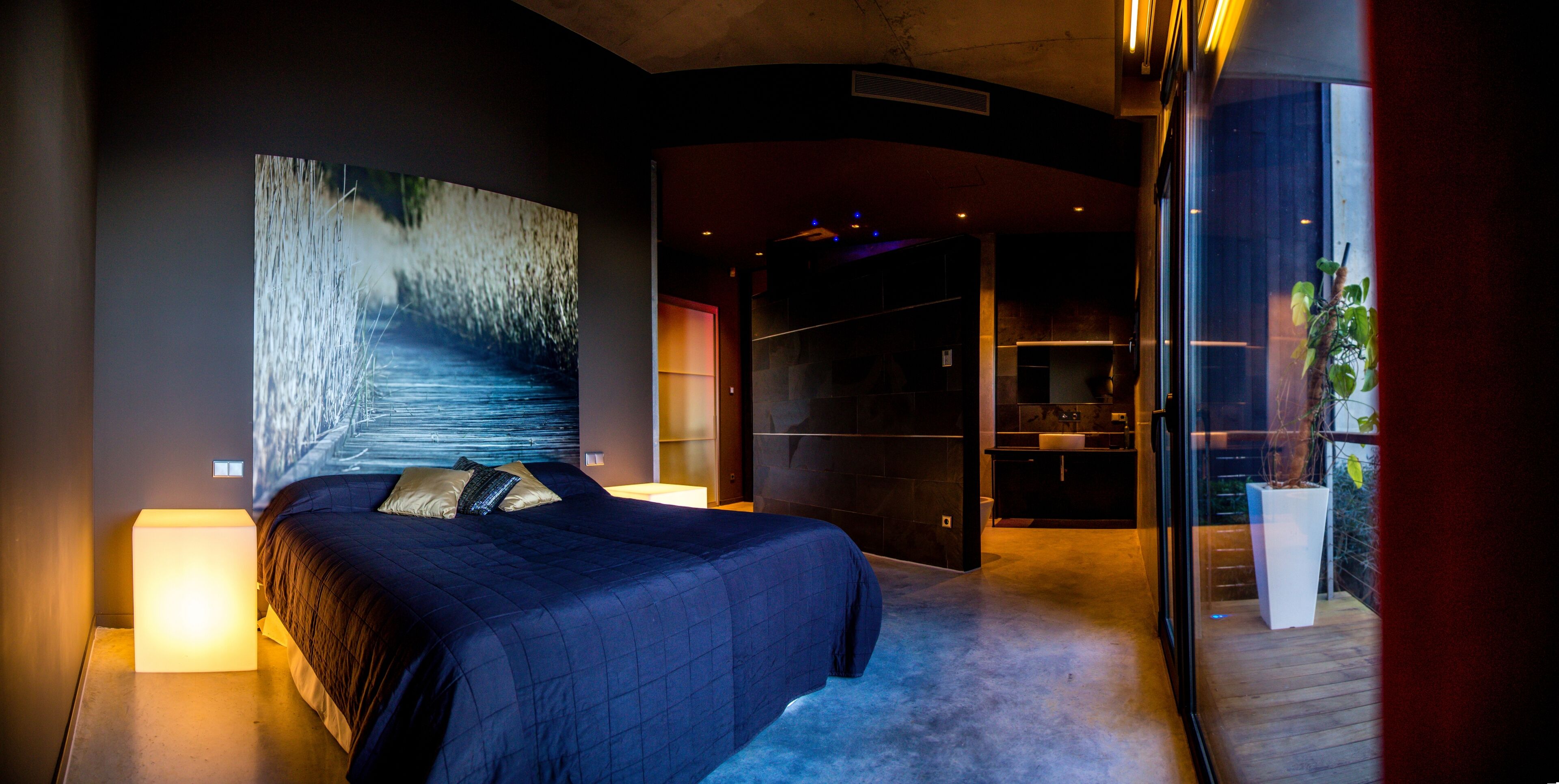 Een moderne slaapkamer met een groot bed, een nachtkastje, een tv aan de muur en een schuifdeur naar een balkon.