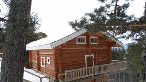 Eine Blockhütte mit Balkon und kleiner Veranda, umgeben von Bäumen und Schnee.