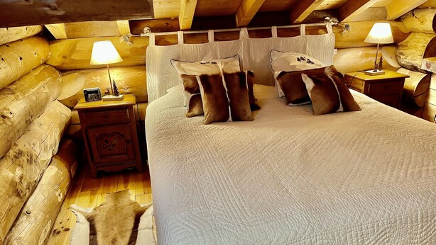 Ein Schlafzimmer in einer Blockhütte mit einem großen Bett, zwei Nachttischen mit Lampen und einem Holzboden.