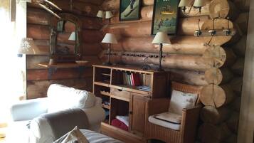 L’intérieur d’un chalet confortable, avec un canapé, un fauteuil, une bibliothèque en bois et des lampes fixées au mur.