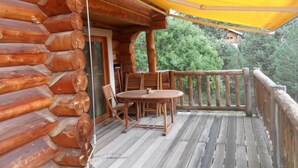 Eine Holzhütte mit Balkon, Sitzgelegenheit im Freien und einem gelben Markisenvorbau.