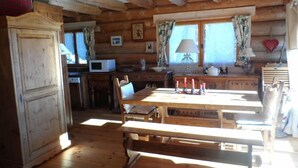 Ein rustikales Blockhaus-Interieur mit Holzwänden und -decken, einem Esstisch mit Bänken, einer Küchenzeile mit Mikrowelle und einem großen Holzschrank.