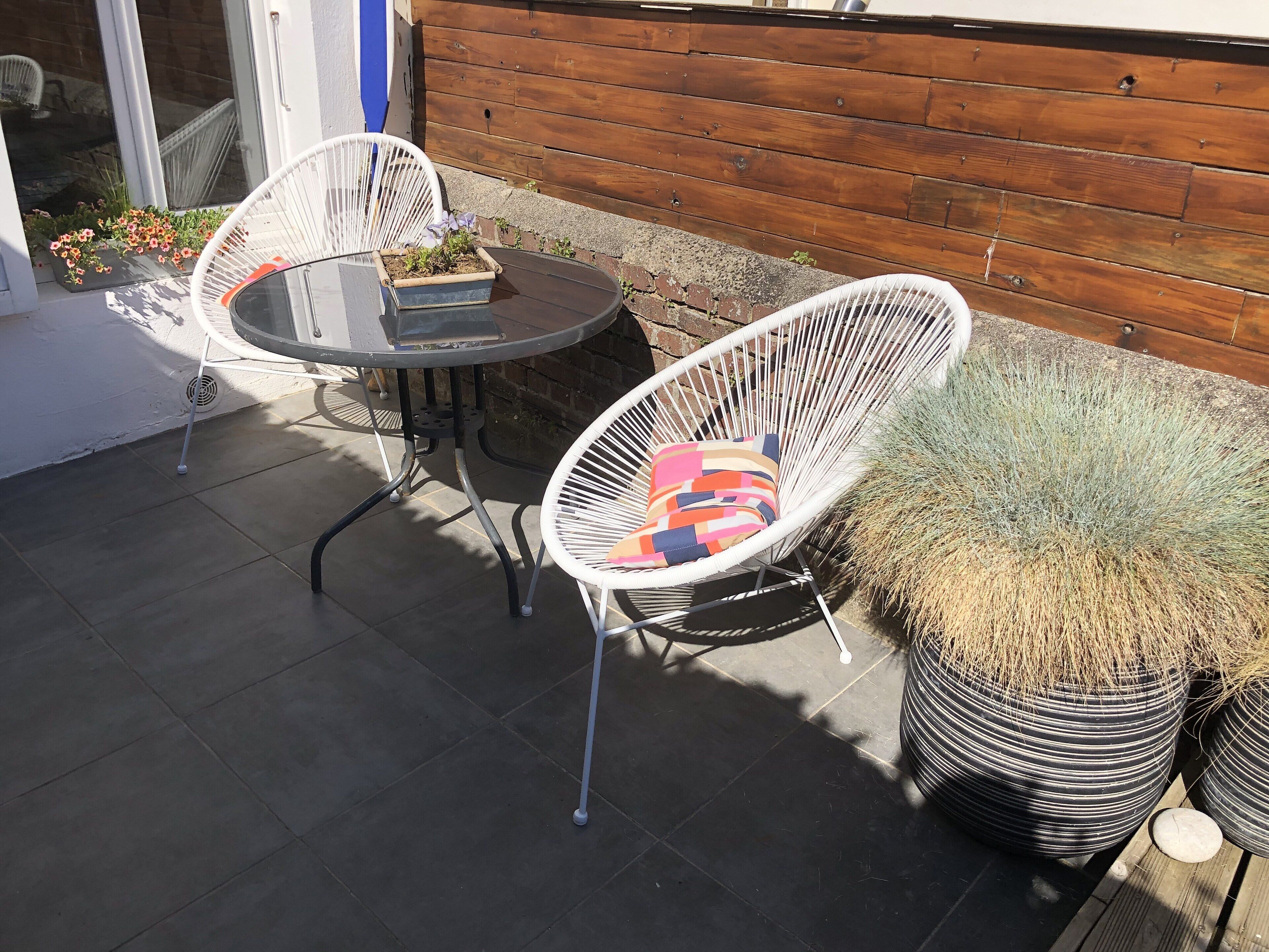 Un patio con due poltrone in vimini bianco, un tavolino rotondo e una pianta in vaso.