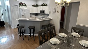 Une cuisine moderne avec des meubles blancs, un îlot central et un coin repas doté d’une table en bois, dressée pour six personnes.