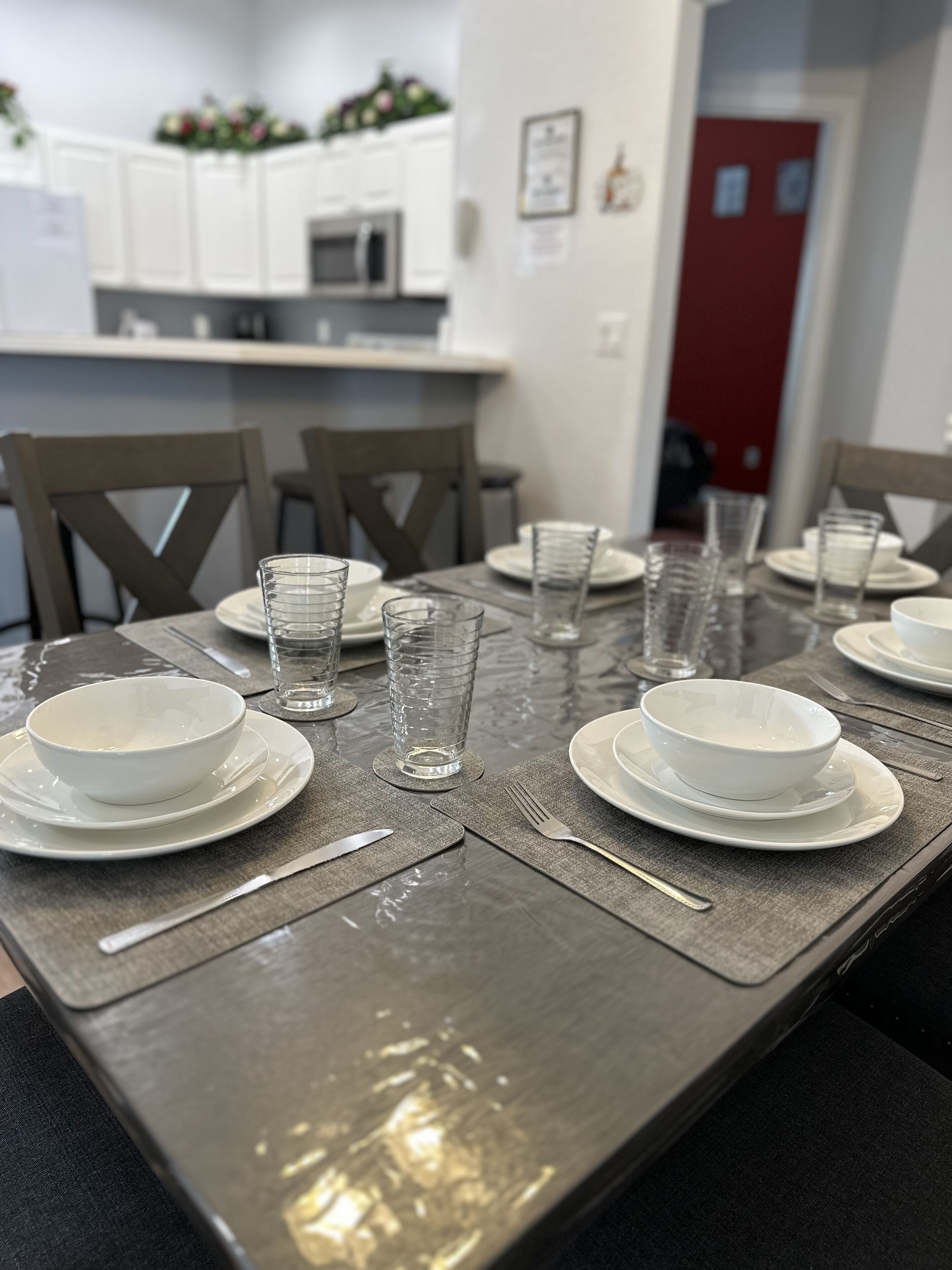 A dining table set with white plates, bowls, and clear glasses, with chairs around it.