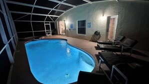 Une piscine intérieure à bords incurvés, entourée d’une zone abritée comprenant des chaises et une échelle.