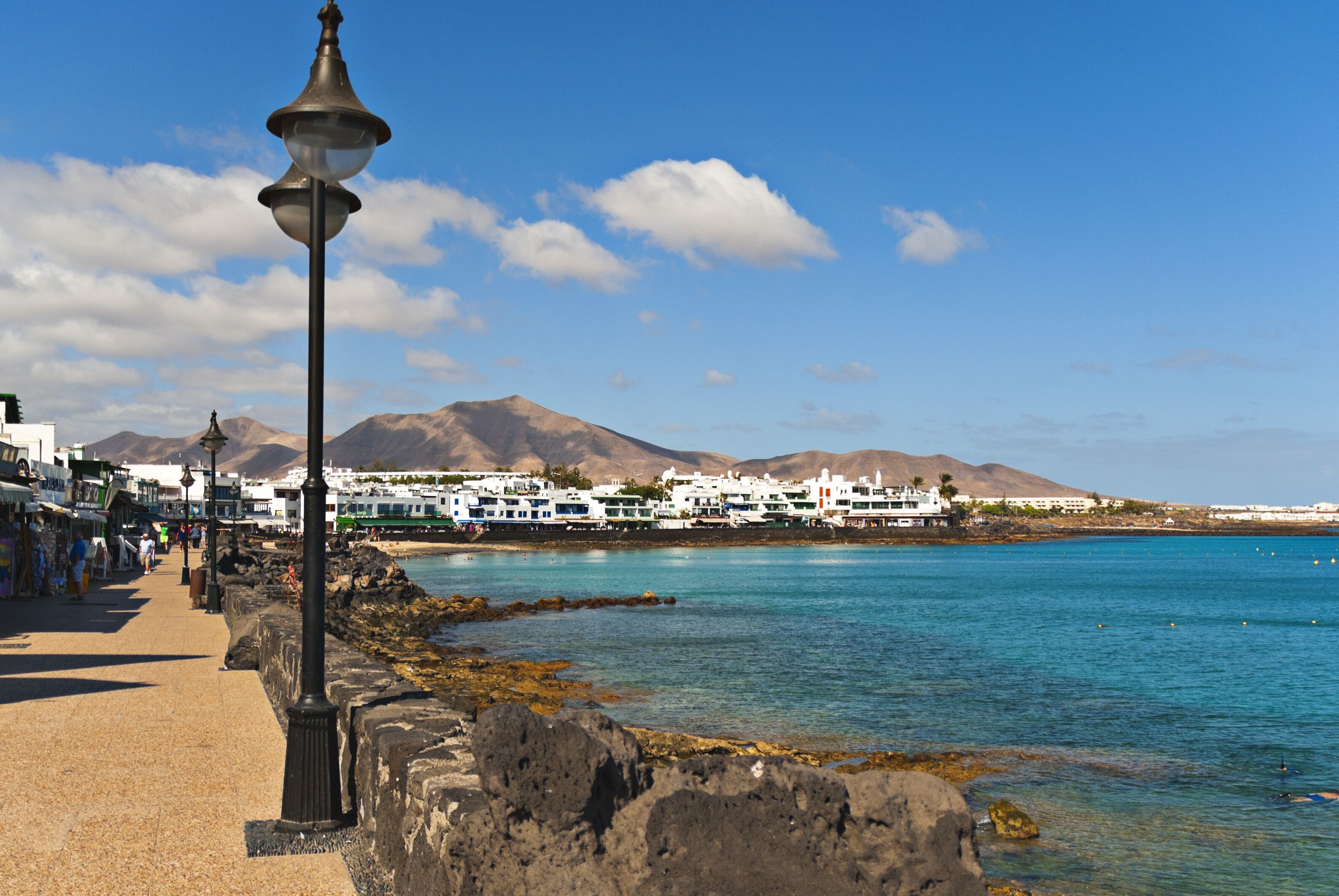 A coastal walkway with a stone balustrade, a street lamp, and buildings in the background.