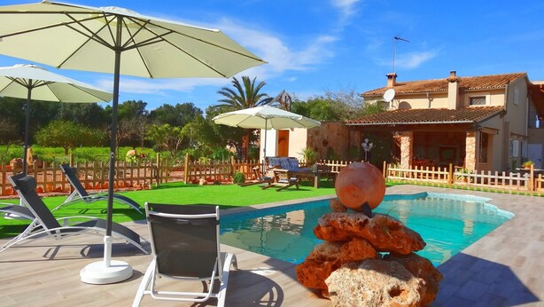 A pool area with lounge chairs and umbrellas, a stone sculpture, and a house in the background. - Son Antem, Air Conditioning, Wifi free, Private pool, 8 km From Cala Blava (Llucmajor)