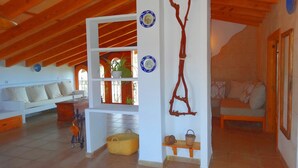 A spacious living room with a high ceiling, wooden beams, a white wall with decorative plates, a sofa, and a bench. - Son Antem, Air Conditioning, Wifi free, Private pool, 8 km From Cala Blava (Llucmajor)