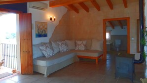 A living room with a sofa, a wooden ceiling, a painting, and a bathroom visible through an open door. - Son Antem, Air Conditioning, Wifi free, Private pool, 8 km From Cala Blava (Llucmajor)