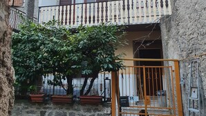 A two-story stone building with a balcony, potted plants, and a gate.