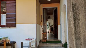 A narrow hallway with a wooden door leading to a room, a small table with a book, and a potted plant.