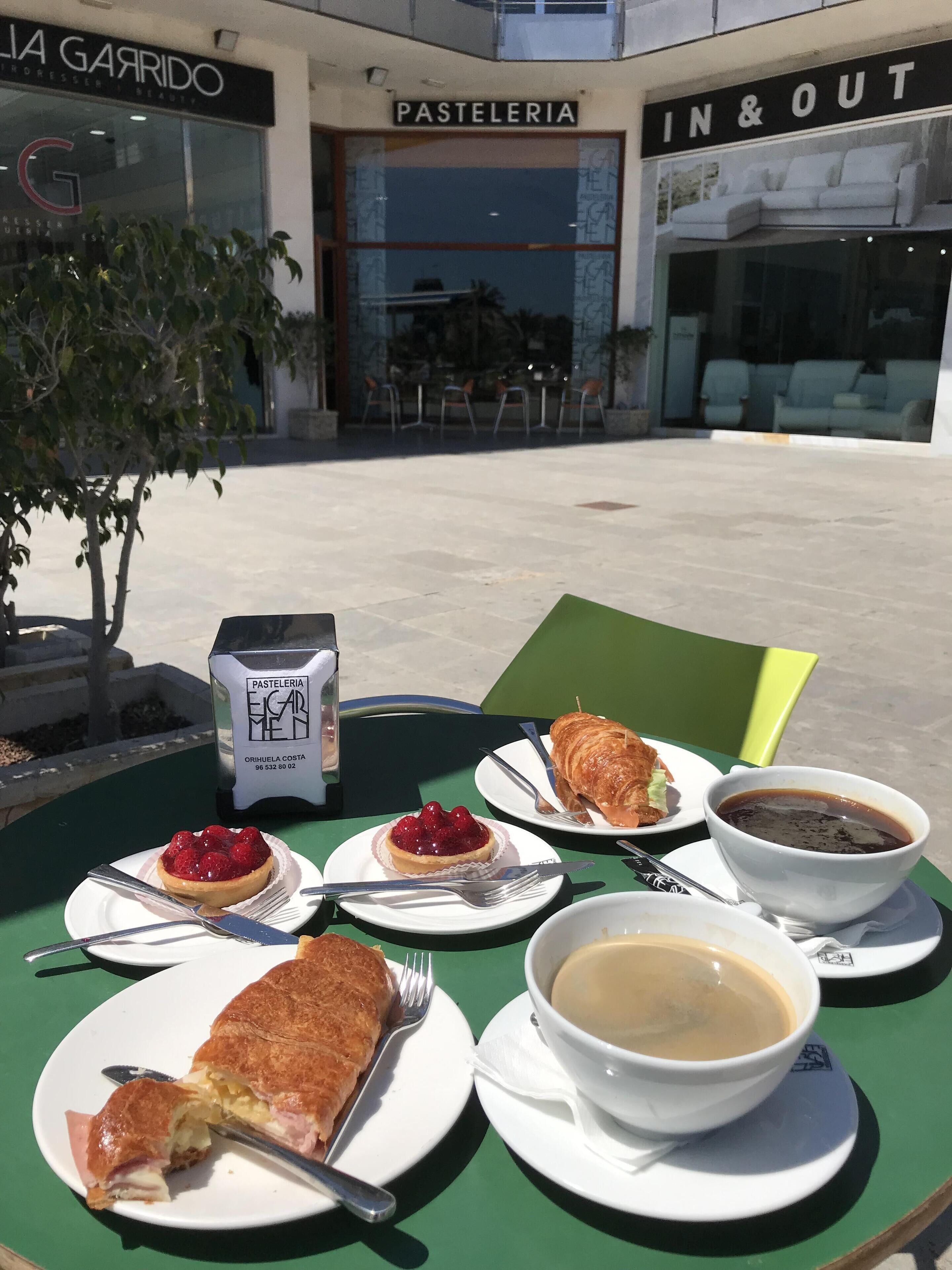 Een tafel met eten en een drankje voor een gebouw met een etalage waarop 'PASTELERIA' staat.