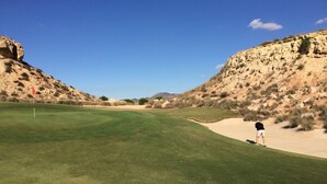 Un campo da golf con cielo sereno, una bandiera a sinistra e una buca di sabbia a destra.