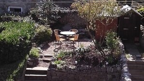 A stone building with a garden patio featuring a table and chairs, surrounded by plants and a brick wall.