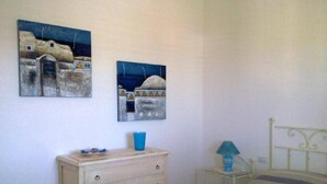 A bedroom with a bed, a dresser, a nightstand, a lamp, and two paintings on the wall.
