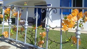 A house with a white exterior and blue shutters, a metal fence with flowers, and a clear blue sky.