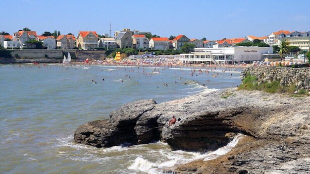 Une ville côtière avec un littoral rocheux, une plage et des bâtiments aux toits rouges.