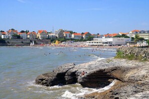 A coastal town with a rocky shoreline, beach, and buildings with red roofs.