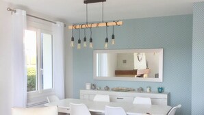 Un espace repas moderne avec une table blanche, des chaises en bois et un luminaire suspendu.