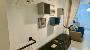 A room with a white wall, a green trunk, a sofa, and a hanging rack with white items.