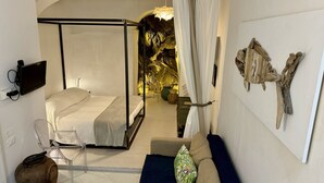 A bedroom with a four-poster bed, a sofa, a TV mounted on the wall, and a decorative wall piece.