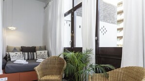 A modern bedroom with a bed, two wicker chairs, a potted plant, and a view of the city through large windows. - CASANOVA ELEGANCE, excellent apartment, excellent location in Barcelona center (Barcelona)
