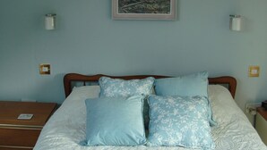 Una camera da letto con un letto, cuscini, un comodino, una lampada e un quadro appeso al muro.
