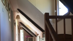 Un corridoio con una scala in legno, un pavimento tappezzato e vista su una stanza con un letto e una finestra.