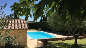 Una piscina con pared de piedra y techo de tejas, rodeada de grava y plantas en macetas.