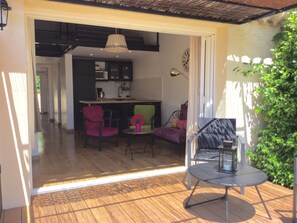 An open-plan living area with a wooden floor, a dining table, and several chairs. There is a kitchen area visible in the background. - GITE PRES DU JASMIN with SWIMMING POOL and GARDEN / SPECIAL W.E. OFFER OF MAY (Rasteau)