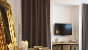 Una habitación de hotel con una cama, un televisor montado en la pared, una bandeja con dos tazas, un espejo decorativo y cortinas.