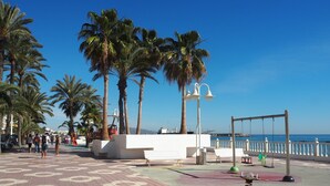 Ein gepflasterter Weg mit Palmen, einem Spielplatz und Blick aufs Meer.