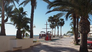 Ein gepflasterter Weg mit Palmen, einem Spielplatz und Blick auf das Meer.