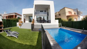 Ein modernes, zweistöckiges Haus mit Swimmingpool, gepflegtem Rasen und einem Balkon.