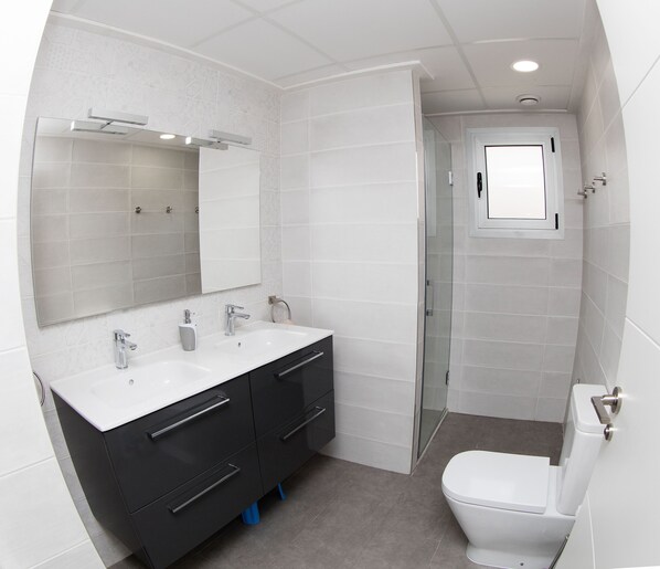 Une salle de bain moderne avec un grand miroir, deux lavabos, des toilettes et un espace douche.