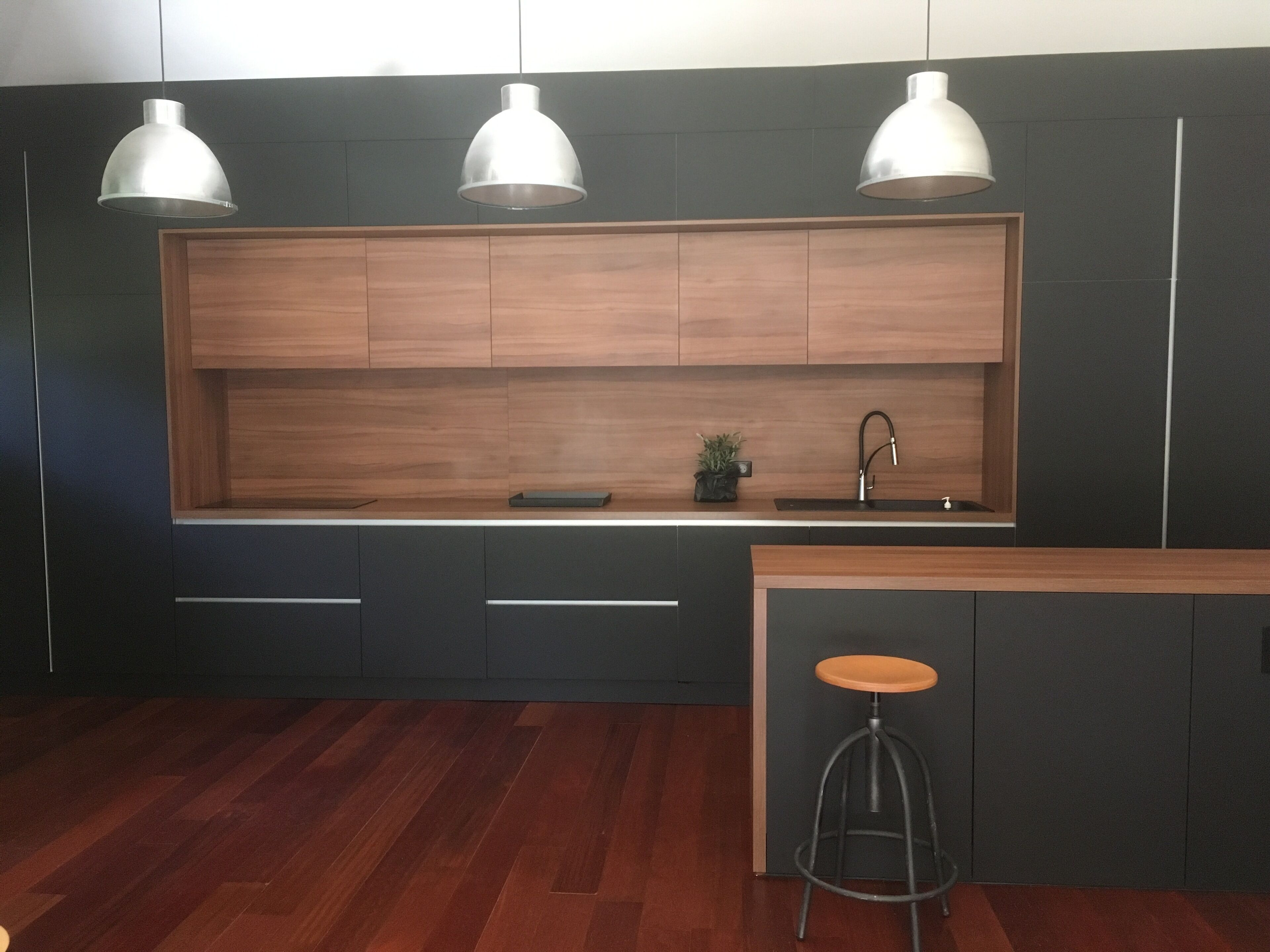 A modern kitchen with dark cabinetry, a wooden countertop, a sink, and three pendant lights.