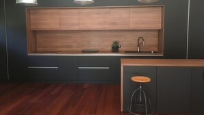 Una cocina moderna con armarios oscuros, encimera de madera, un lavabo y tres lámparas colgantes.