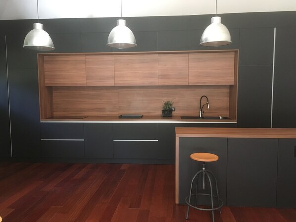 A modern kitchen with dark cabinetry, a wooden countertop, a sink, and three pendant lights. - Large 320m2 villa, fully air-conditioned, heated swimming pool, 5000m2 enclosed garden (Ste Lucie de Porto Vecchio)