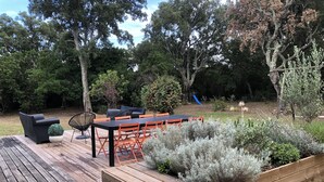 Una terraza de madera con una mesa y sillas, rodeada por un jardín con diversas plantas.