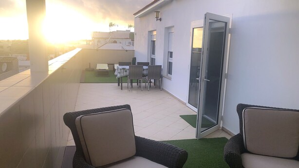 A balcony with wicker chairs, a table, and a door leading to a covered outdoor area with a table and chairs.