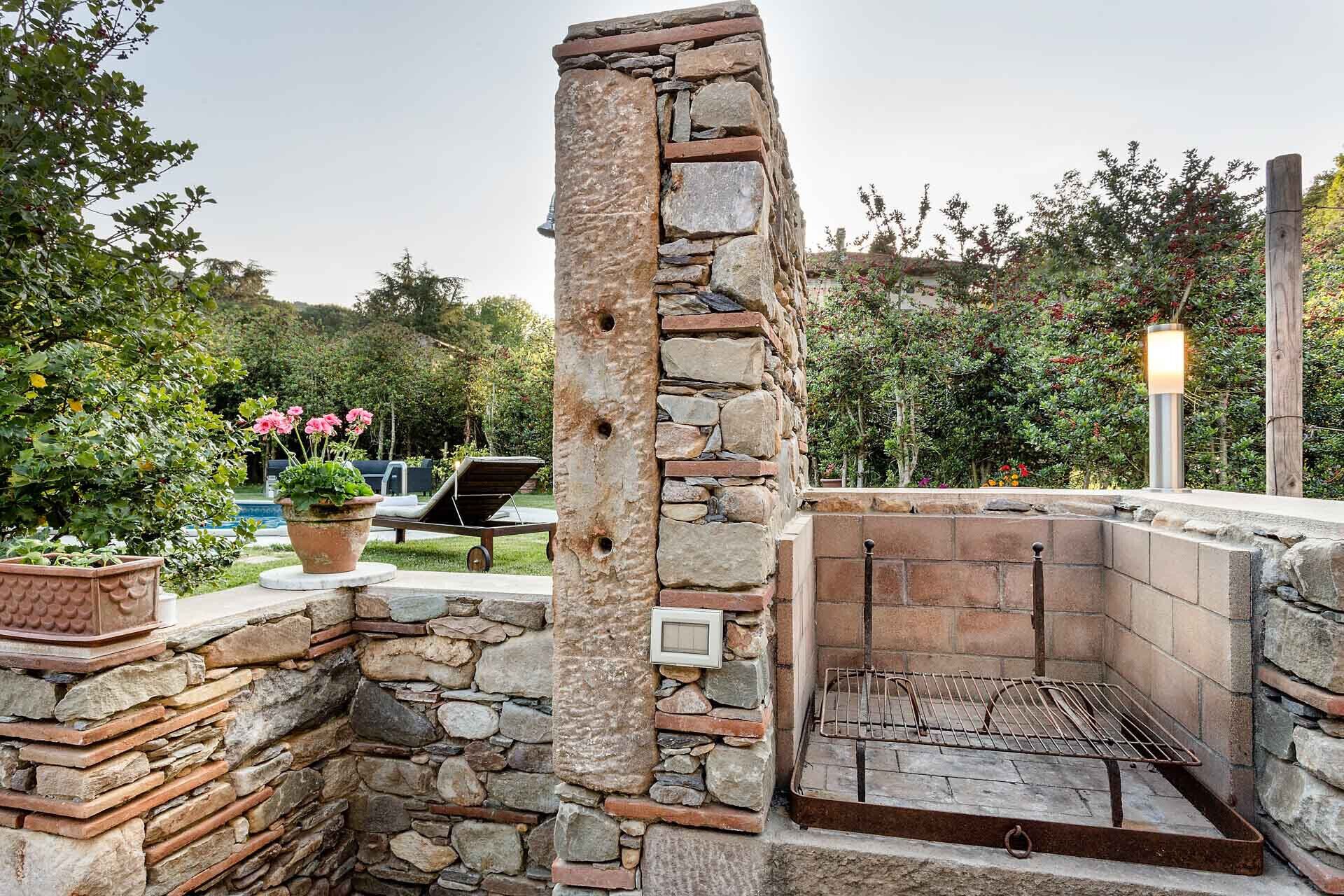 A stone barbecue grill with a stone wall and a potted plant nearby.