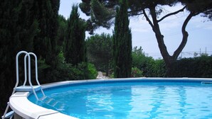 A swimming pool with a curved edge, surrounded by trees and shrubs.