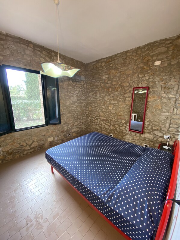 A bedroom with a stone wall, a large window, a bed with a polka dot bedspread, and a mirror.
