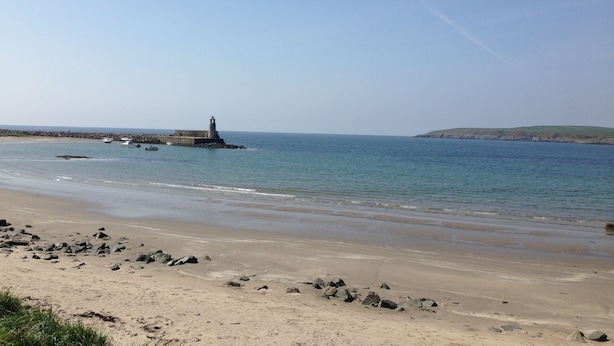 Una playa con un faro, agua tranquila y una colina distante.