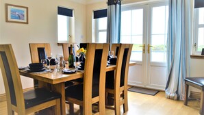 Un comedor con una mesa de madera dispuesta para cuatro personas, sillas y una ventana con cortinas.