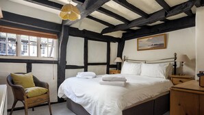 Ein Schlafzimmer mit einem großen Bett, einem Sessel, einem Nachttisch und einem Fenster mit Jalousien.