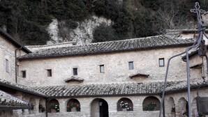Un pati amb paviment de pedra, un edifici amb múltiples arcs i una paret de pedra rústica.